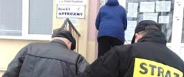 Na zdjęciu strażak OSP w ubraniu koszarowym pomaga wejść po schodach starszej osobie do przychodni NFZ.