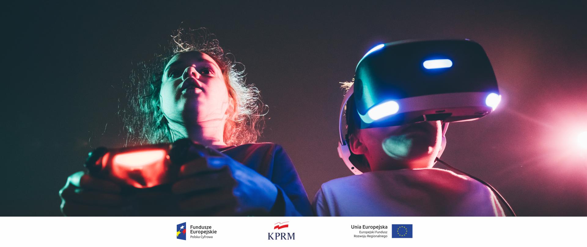 Dwoje dzieci grających w gry cyfrowe. Dziewczynka (z lewej) trzyma w dłoniach pad. Chłopiec (z prawej) ma na sobie okulary VR.