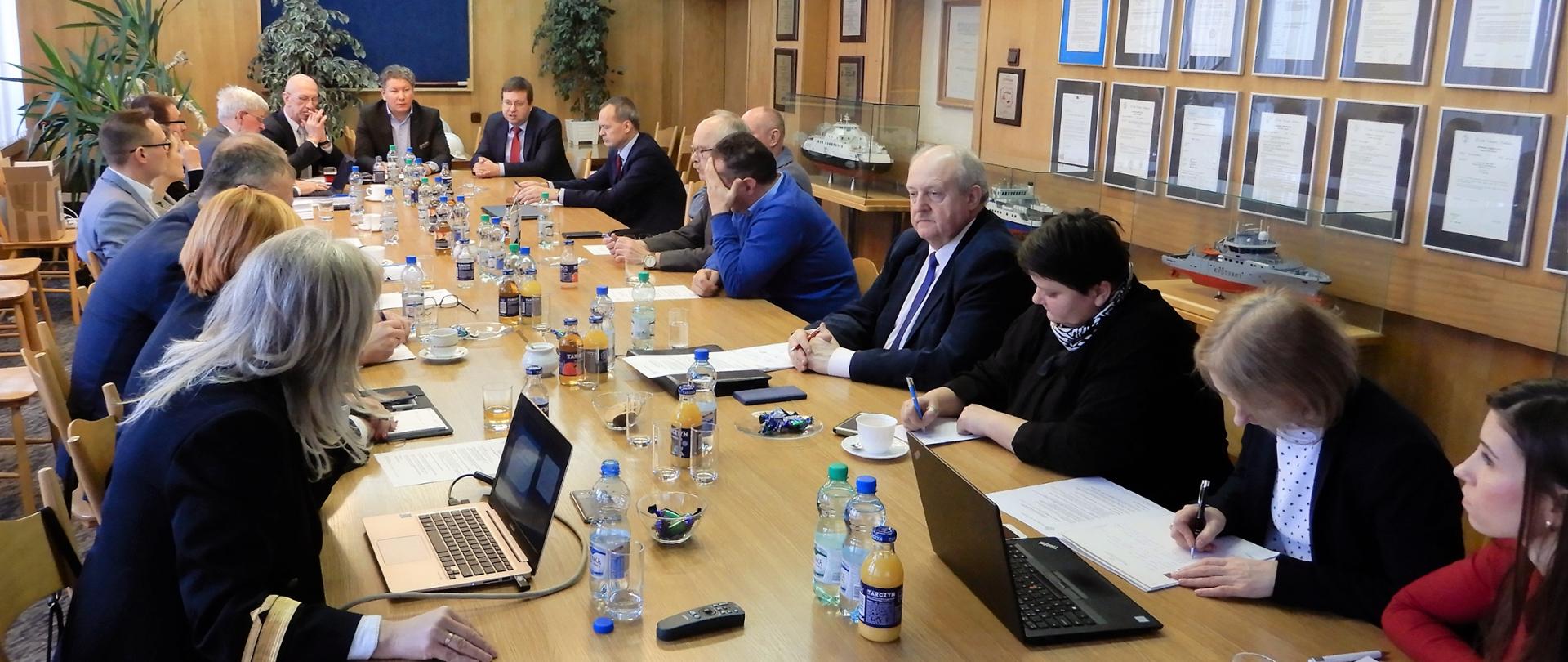 Uczestnicy spotkania siedzą przy wspólnym stole, słuchając prelegenta