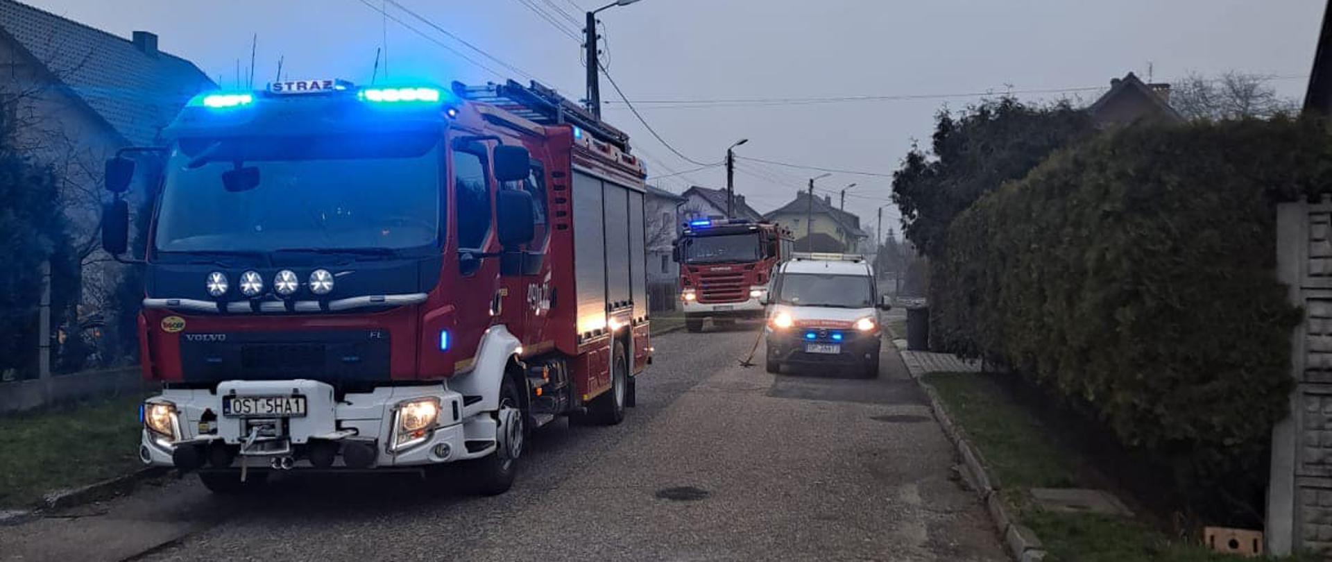 Na zdjęciu znajdują się samochody strażackie oraz pogotowia gazowego, w tle widać zabudowania