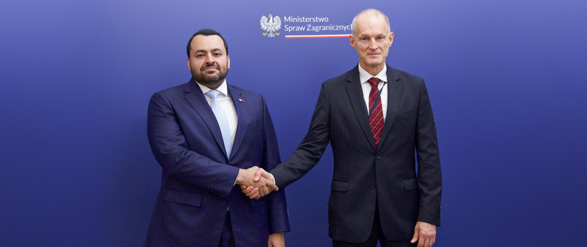Podsekretarz Stanu w MSZ Wojciech Zajączkowski wymienia uścisk dłoni z Ministrem Stanu w Ministerstwie Spraw Zagranicznych Państwa Katar Mohammedem bin Abdulazizi al-Khulaifim w Warszawie. Na granatowym tle z logo Ministerstwa Spraw Zagranicznych.