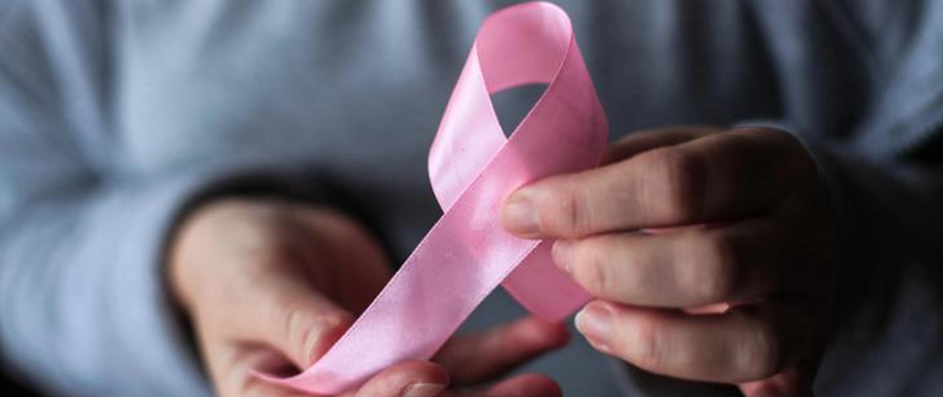 Obraz przedstawia osobę trzymającą różową wstążkę w dłoniach jako symbol walki z rakiem piersi