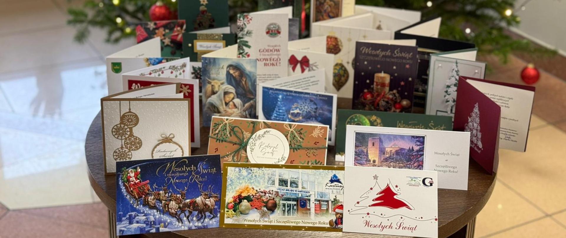 Zdjęcie przedstawia kartki z życzeniami otrzymane od zaprzyjaźnionych instytucji oraz firm. W tle choinka