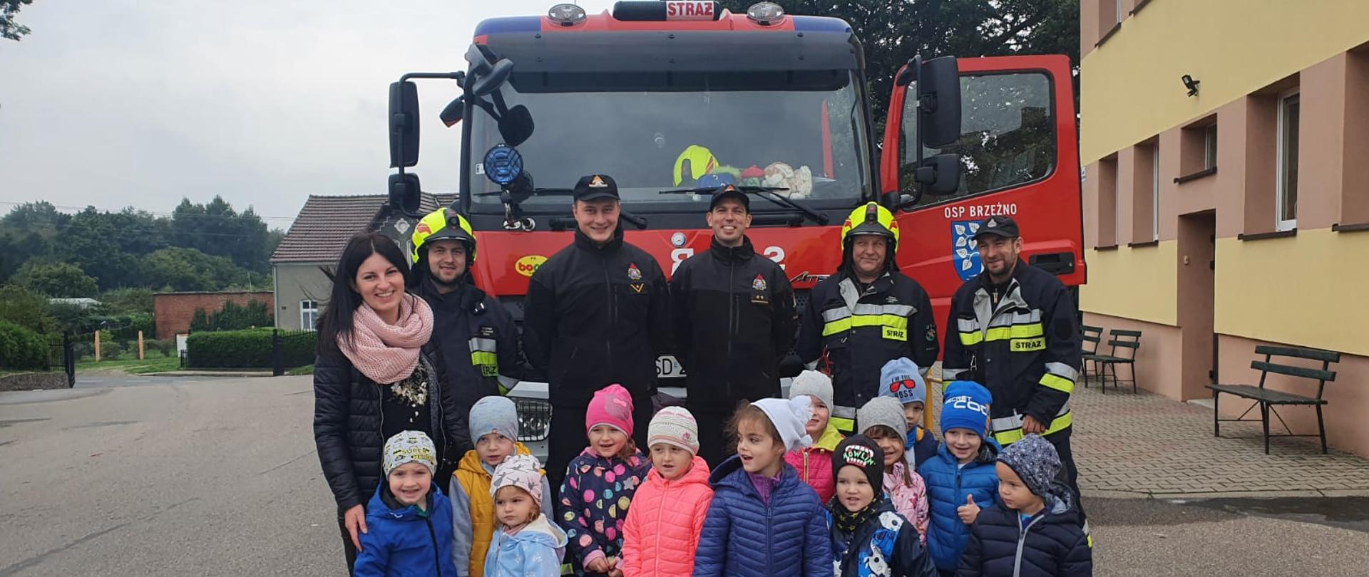 Zdjęcie przedstawia grupę przedszkolaków oraz strażaków na tle wozu strażackiego.