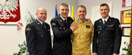 4 umundurowanych strażaków w pomieszczeniu biurowym, w tle flagi oraz godło państwowe