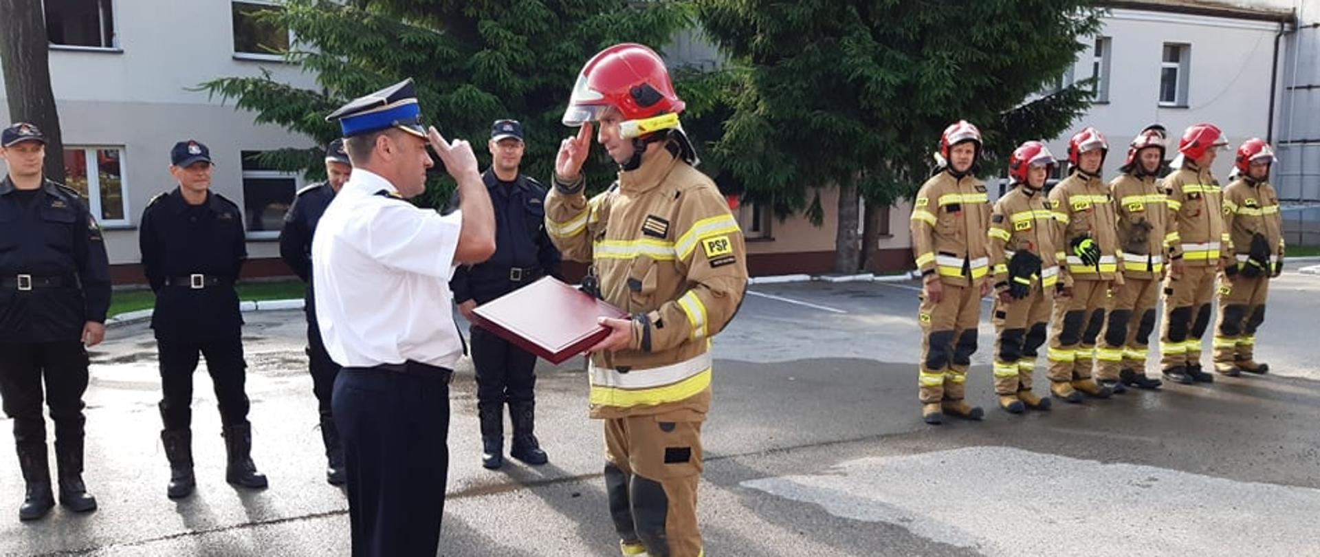 Uroczysta zmiana służby. Na środku stoi komendant i strażak oddając honor.