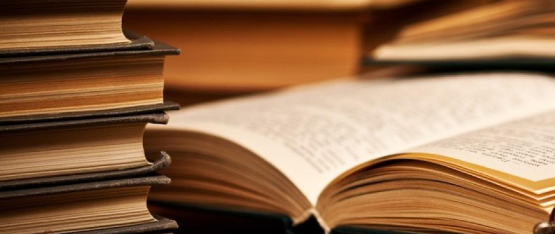 Książki ułożone w stos, obok jedna książka otwarta