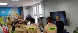 Młodzież w sali edukacyjnej słucha przemówienia strażaków.