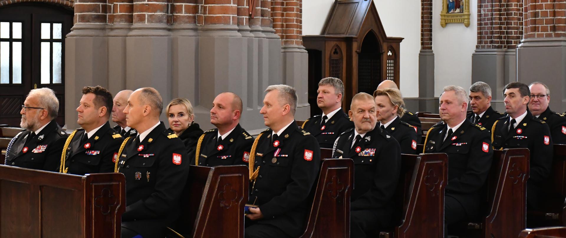Uczestnicy uroczystości w czarnych mundurach wyjściowych siedzą w kościelnych ławach.