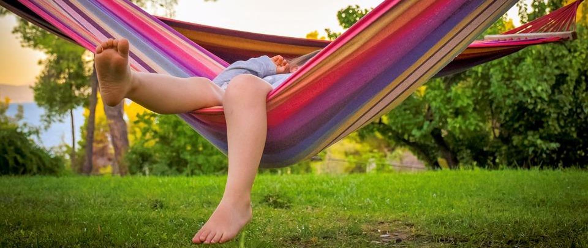 Dziecko leży w kolorowym hamaku, w tle zielone rośliny