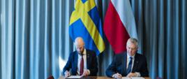 Ministrowie Siemoniak i Bohlin podpisują dokumenty na tle flag polskiej i szwedzkiej 