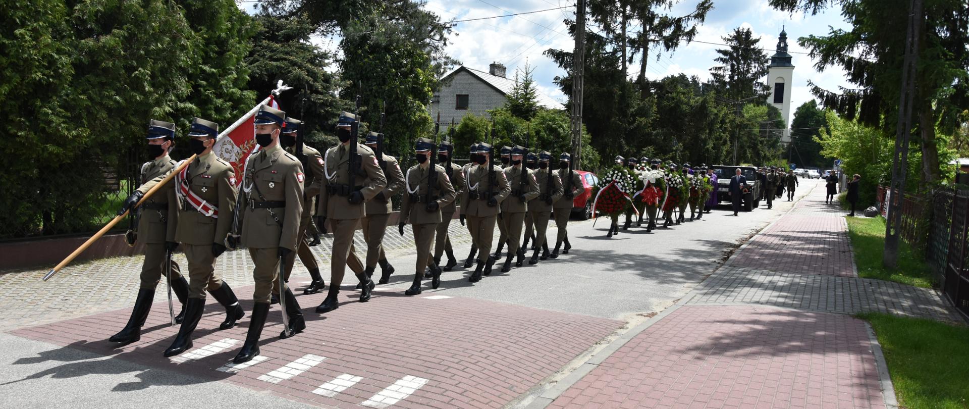 Kondukt pogrzebowy idący ulica od kościoła w stronę cmentarza. Na pierwszym planie kilkunastu żołnierzy idących jako asysta wojskowa. 