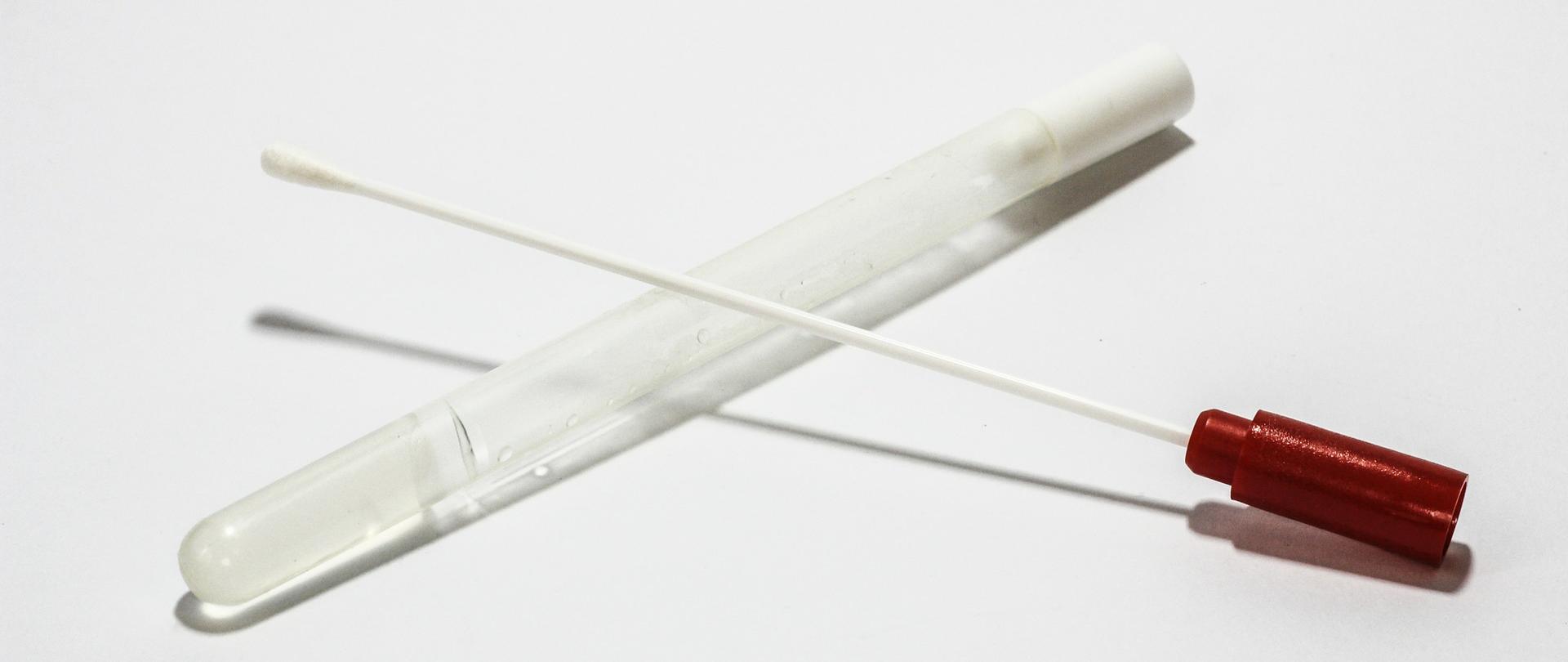 Otwarta probówka (wymazówka). Na probówce z podłożem transportowym leży patyczek z umieszczonym na końcu wacikiem. 