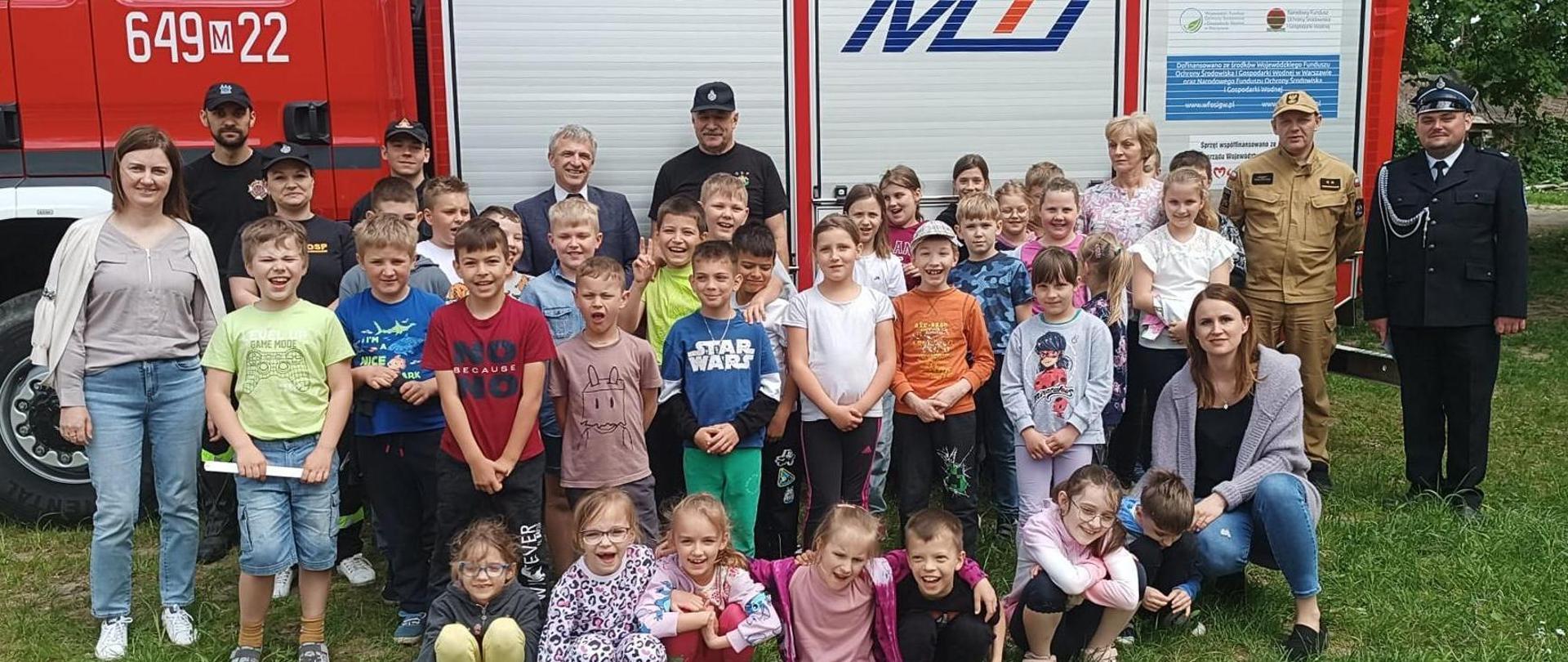 Spotkania sokołowskich strażaków z dziećmi. 6-7.05.2024 - wspólne zdjęcie strażaków z uczniami przed samochodem strażackim