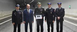 Zdjęcie przedstawia Prezydenta Miasta Świnoujście wraz z funkcjonariuszami PSP. od lewej: Zastępca Zachodniopomorskiego Komendanta PSP st. bryg. Mirosław Pender, Prezydent Miasta Janusz Żmurkiewicz, Zachodniopomorski Komendant PSP nadbryg. Jarosław Tomczyk, st. bryg. Robert Tarczyński, Komendant Miejski PSP w Świnoujściu st. kpt. Marek Wieczorek.
Zebrani stoją na jezdni tunelu.