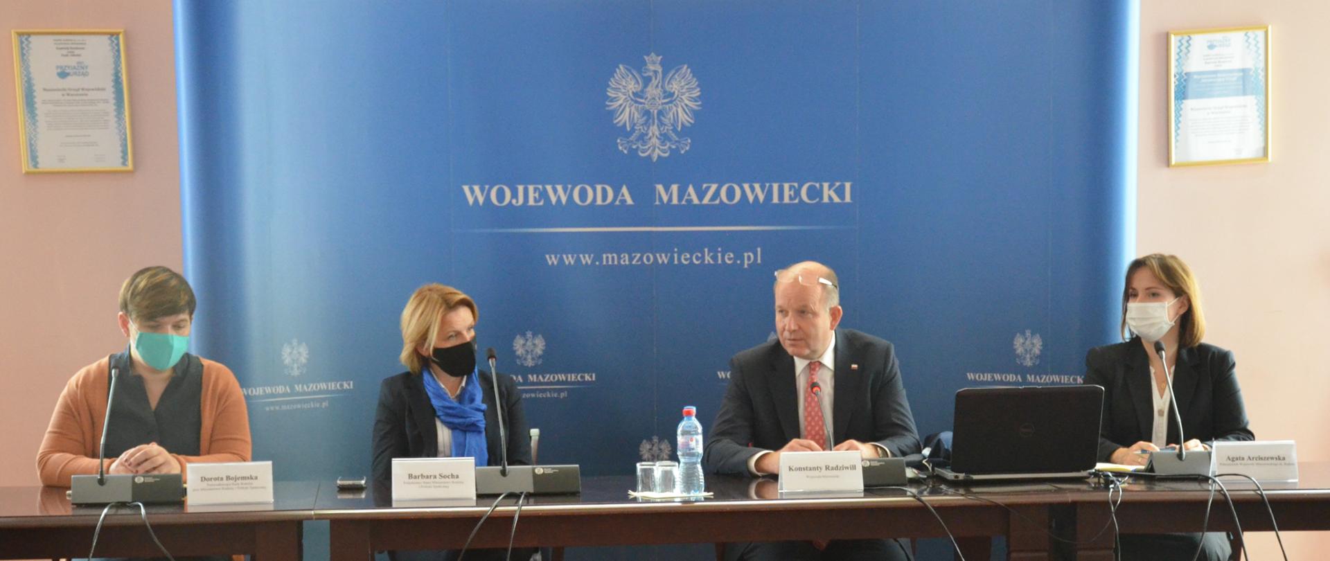 Na zdjęciu znajdują się cztery osoby, w tym jeden mężczyzna siedzący za stołem