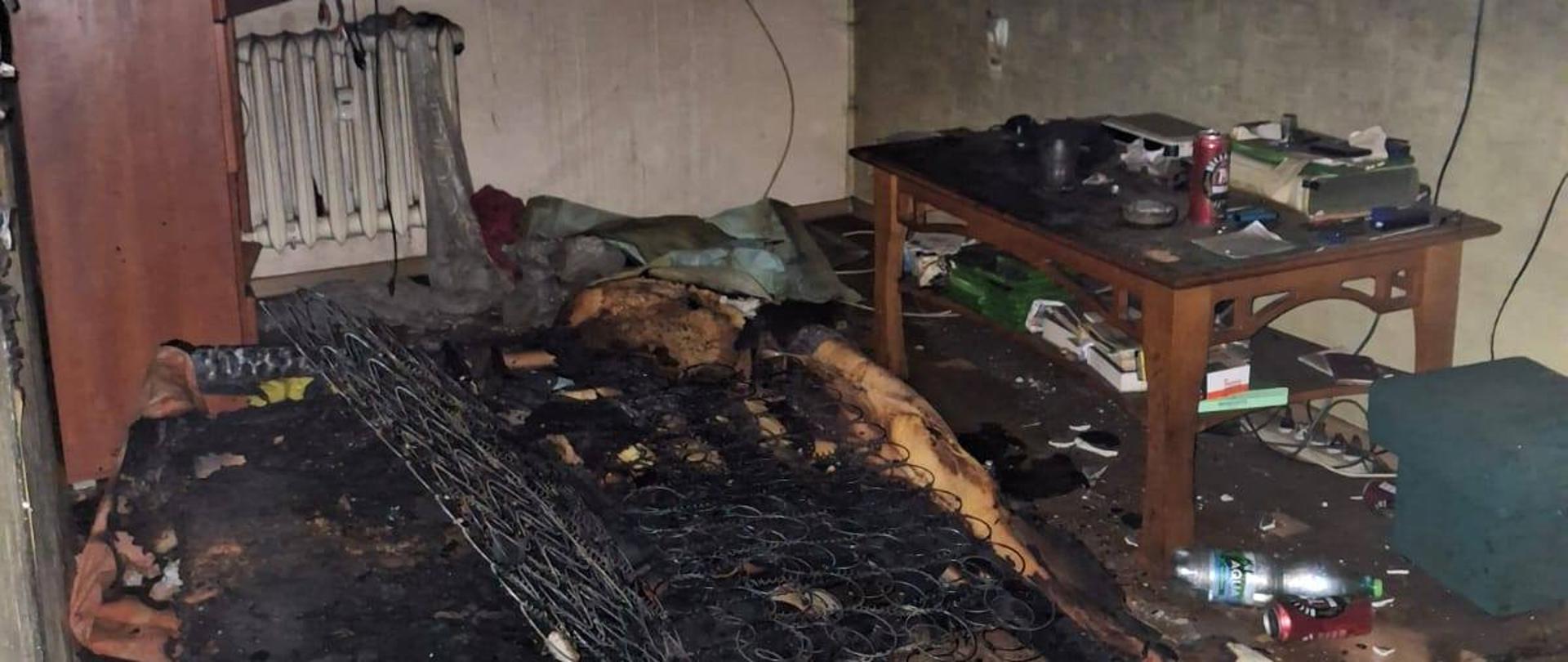 Spalone wnętrze mieszkania, kanapa, stół, szafa, ślady pożaru na ścianach