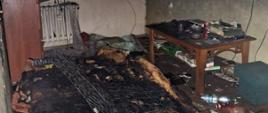 Spalone wnętrze mieszkania, kanapa, stół, szafa, ślady pożaru na ścianach
