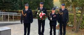 Zdjęcie przedstawia kierownictwo KM PSP w Częstochowie oraz przedstawiciela emerytów podczas składania kwiatów przed pomnikiem. Funkcjonariusze w umundurowaniu wyjściowym