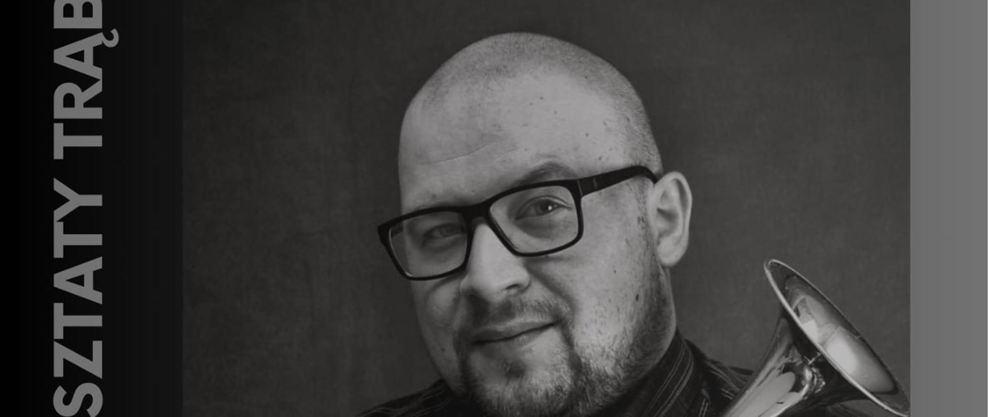 Plakat Warsztatów trąbkowych z Marcinem Olkowskim w dniu 8 grudnia 2025. Tło plakatu jest srebrno-grafitowe, a w jego centralnej części znajduje się czarno-białe zdjęcie pana Marcina, który trzyma przytuloną do siebie trąbkę zwróconą czarą dźwiękową do góry. Trębacz lekko się uśmiecha, ubrany jest w czarną koszulę w szarą paskową kratę, na nosie ma okulary. Napisy informacyjne umieszczone w górnej i dolnej części plakatu maja kolor srebrny i limonkowy.