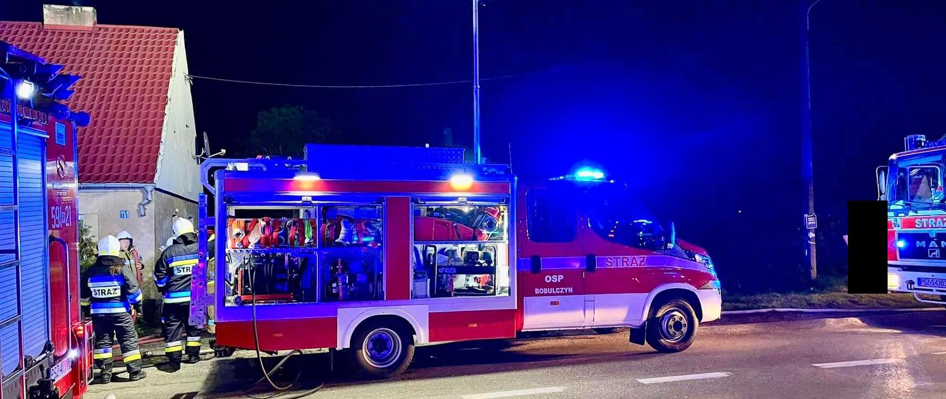 Samochód strażacki przed budynkiem, jest noc