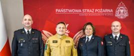 Na tle banneru Państwowej Straży Pożarnej, godła Rzeczypospolitej Polskiej i Flag RP stoją: Opolski Komendant Wojewódzki PSP w Opolu st. bryg. Krzysztof Kuśmierski, mł. kpt. Jolanta Giercuszkiewicz, mł. kpt. Łukasz Nowak i mł. kpt. Karol Widacha. Funkcjonariusze w dniu 14 listopada 2022 roku byli promowani na pierwszy stopień oficerski PSP. Strażacy w umundurowaniu wyjściowym. OKW PSP w Opolu w umundurowaniu służbowym.
