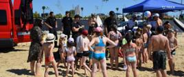 Na zdjęciu strażacy i policjanci oraz dzieci podczas pogadanki na plaży