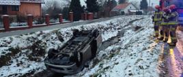 Samochód na dachu w potoku a obok stoją strażacy