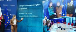 Minister funduszy i polityki regionalnej Katarzyna Pełczyńska-Nałęcz stoi na scenie, za jej plecami ekran z fotografiami na której jest minister Katarzyna Pełczyńska-Nałęcz i Komisarz ds. Polityki Regionalnej Elisa Ferreira