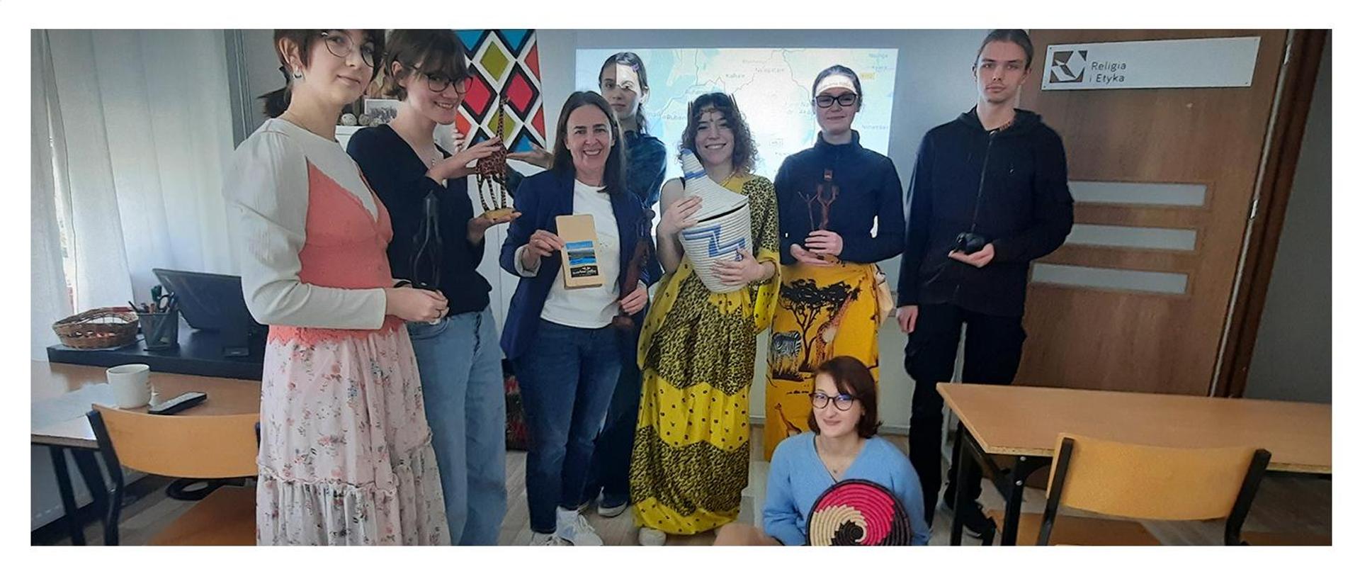 grupa uczniów z nauczycielem przebranych w stroje afrykańskie i trzymających różne przedmioty związane z kulturą afrykańską