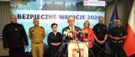 Bezpieczne wakacje 2026 - briefing prasowy. Marek Cebula Wojewoda Lubuski przemawia do mikrofonu. W tle przedstawiciele służb i instytucji oraz grafika "Bezpieczne wakacje"