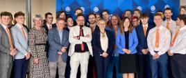 Zdjęcie zbiorowe, pod niebieską ścianką stoi duża grupa osób, pośrodku wiceminister Mrówczyńska.