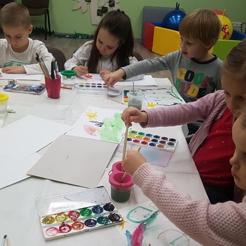 Dzieci siedzące przy stole malują kolorowymi farbkami 