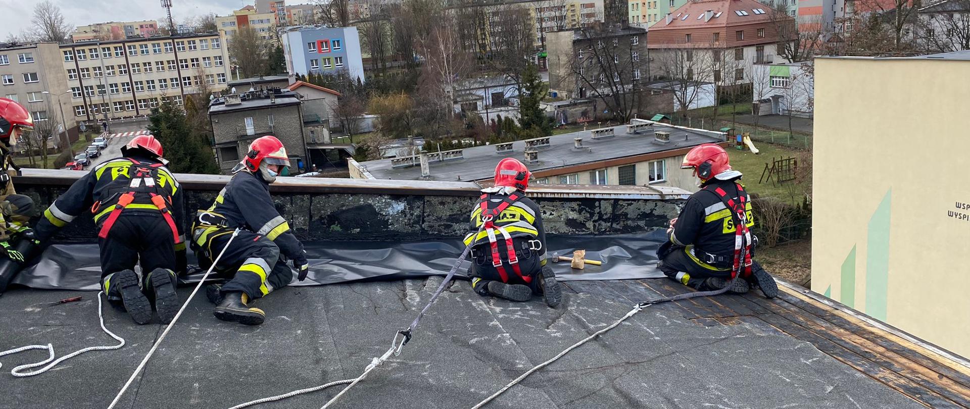 Strażacy w zabezpieczeniach zabezpieczają dach przed działaniami atmosferycznymi