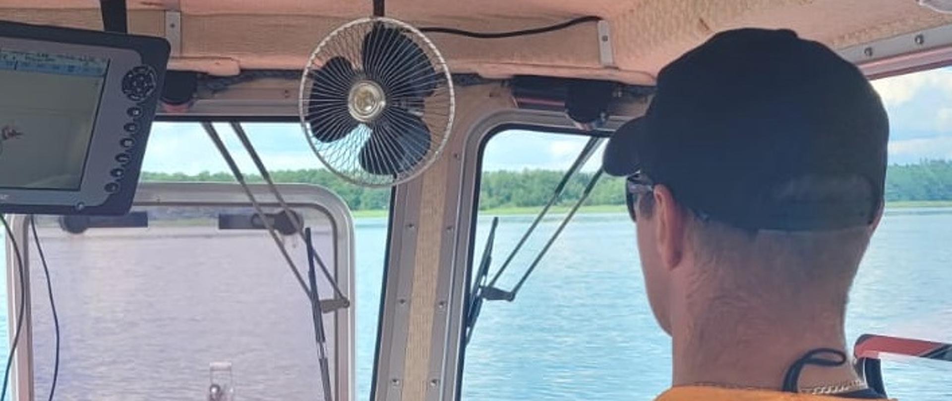 Sternik stoi za sterami ma na sobie założoną kamizelkę Państwowa Straż Pożarna. 