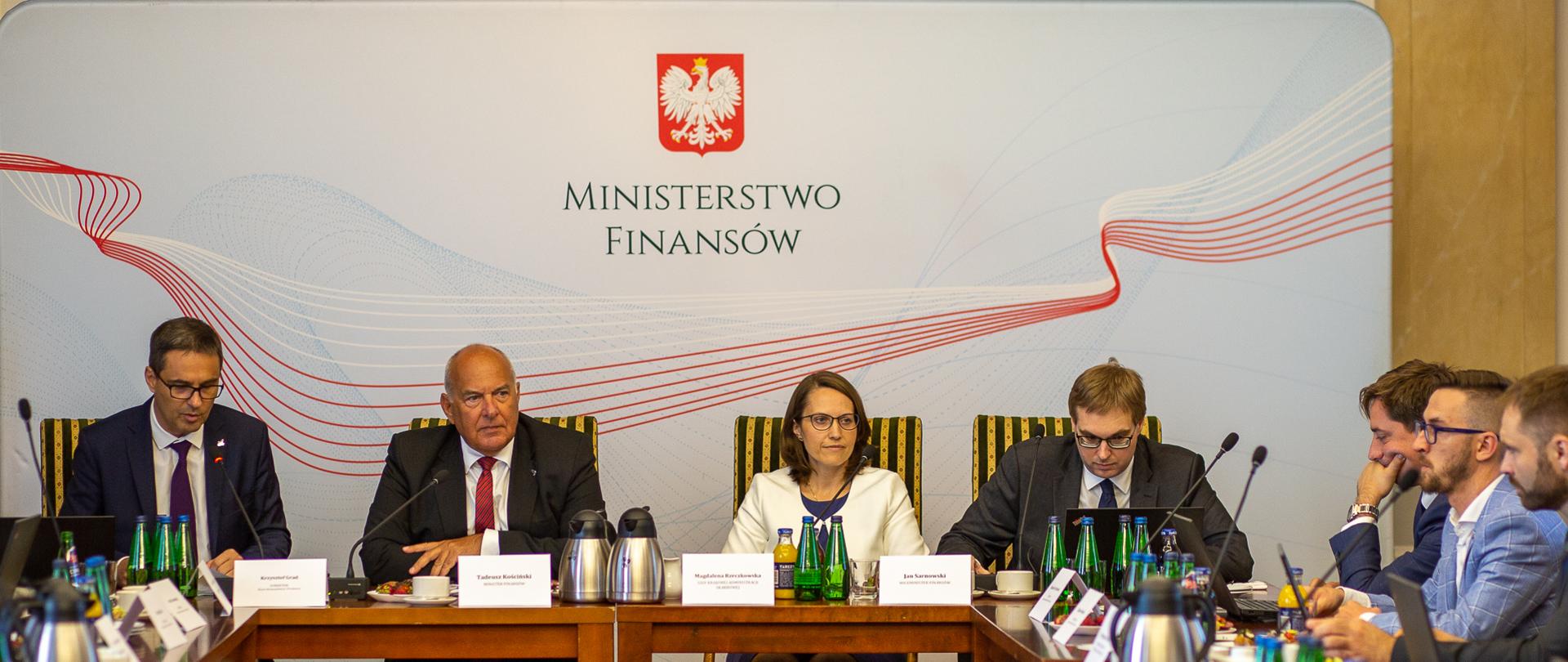 Od lewej: dyr. Biura Komunikacji i Promocji K. Grad, minister T. Kościński, szefowa KAS M. Rzeczkowska i wiceminister J. Sarnowski podczas śniadania prasowego siedzą za stołem, w tle baner z napisem Ministerstwo Finansów