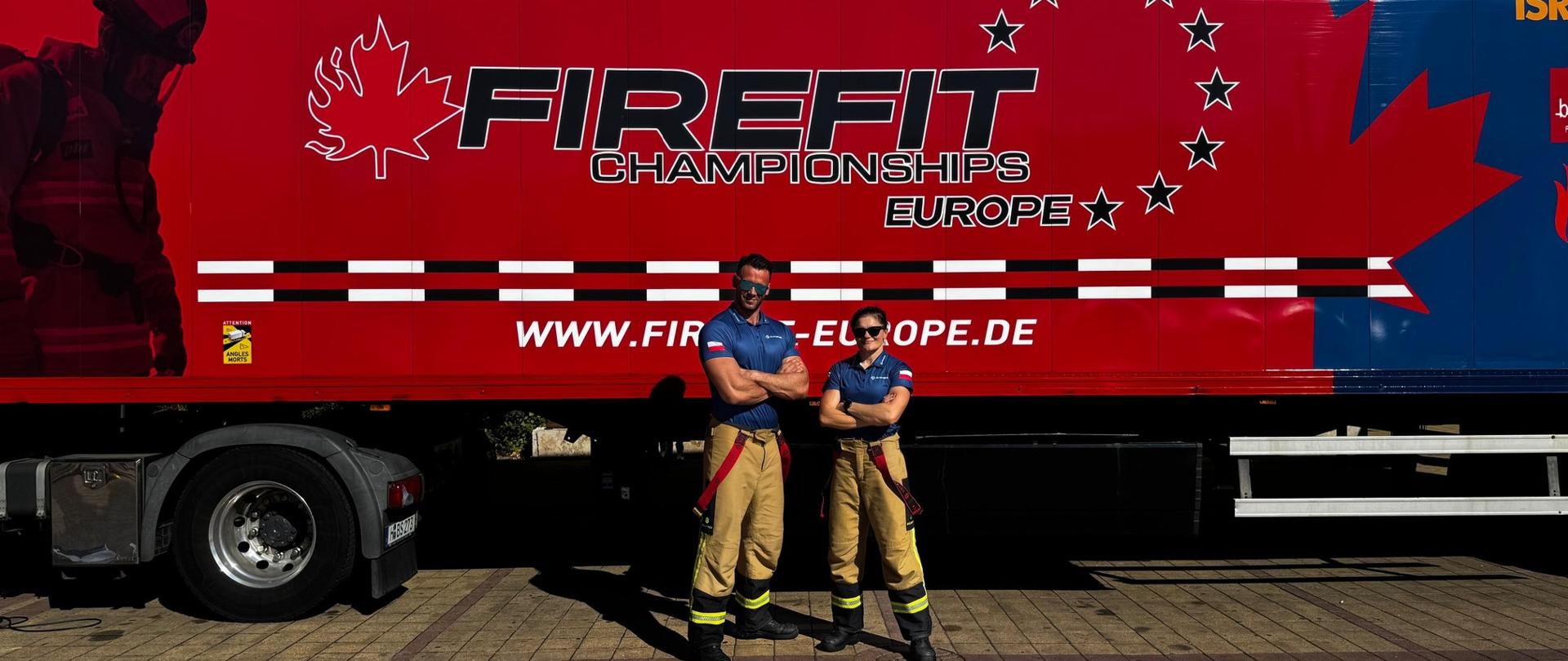 Na zdjęciu widzimy dwie osoby w spodniach strażackich i granatowych koszulkach stojące obok siebie z założonymi rękami. Za nimi znajduje się duża, czerwona naczepa z logo FIRE FIT Championships Europe oraz adresem strony internetowej „www.firefit-europe.de”
. Na grafice widać także sylwetkę strażaka oraz duży liść klonu z gwiazdami ułożonymi w okrąg.