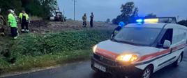 Na zdjęciu widać samochód pogotowia gazowego stojący na drodze wojewódzkiej. W tle na polu stoi ciągnik rolniczy. Na polu widać stojących strażaków i pracowników pogotowia gazowego