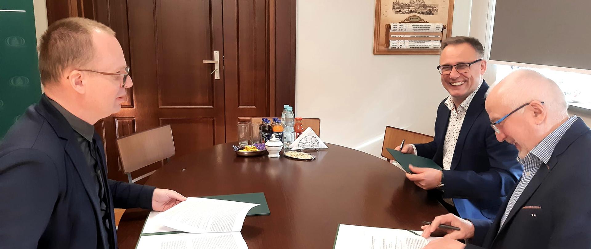 Dyrektor Regionalnej Dyrekcji Ochrony Środowiska w Bydgoszczy Szymon Kosmalski (z lewej strony) podpisał dziś dwie umowy z Prezesem Wojewódzkiego Funduszu Ochrony Środowiska i Gospodarki Wodnej w Toruniu Ireneuszem Stachowiakiem wraz z zastępcą Prezesa Dariuszem Wrzosem (z prawej strony). Podpisanie nastąpiło przy drewnianym stole w siedzibie WFOŚiGW w Toruniu