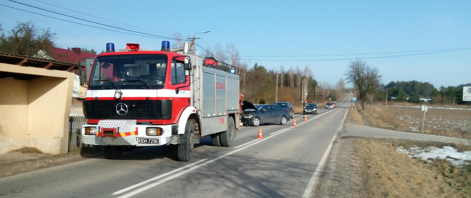 Zdjęcie przedstawia miejsce zdarzenia: Droga Wojewódzka nr 748 wraz z samochodami przybyłych służb oraz uszkodzony samochód Hyundai Elanta biorący udział w zdarzeniu. 