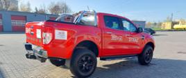 Zdjęcie przedstawia nowy lekki samochód rozpoznawczo - ratowniczy marki FORD. Samochód koloru czerwonego stoi na placu komendy. Z tyłu widać garaże. 