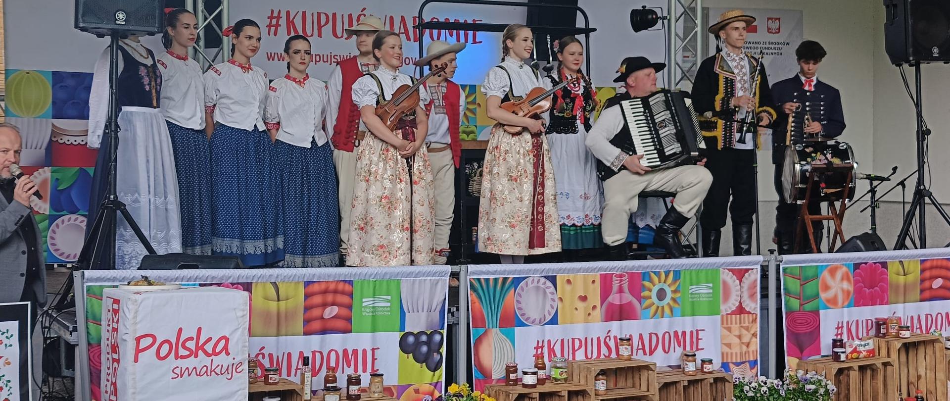 Występ artystyczny na scenie podczas „Zachodniopomorskiego Święta Smaków i Tradycji” w Koszalinie. Artyści prezentują program muzyczny i folklorystyczny, tworząc wyjątkową atmosferę święta, które łączy mieszkańców i gości wokół regionalnej kultury, tradycji oraz wspólnego celebrowania dziedzictwa Pomorza Zachodniego.