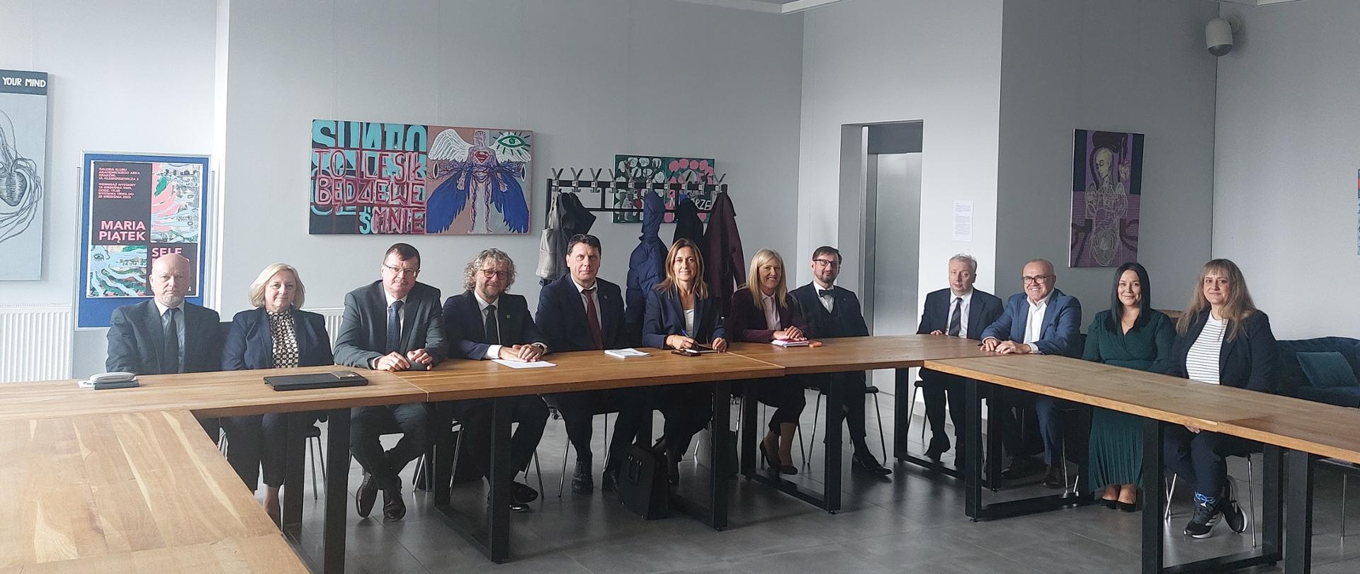 Grupa osób, kobiet i mężczyzn siedząca przy stołach na sali