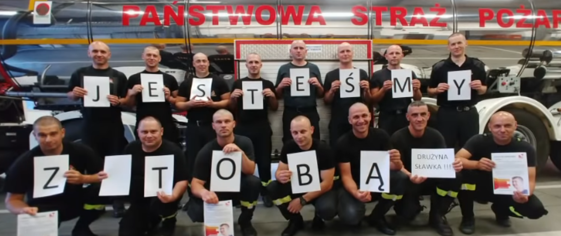 Strażacy trzymający w rękach napis: Jesteśmy z Tobą