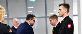 Sekretarz stanu w Ministerstwie Infrastruktury gratuluje druhowi ochotniczych straży pożarnych, obok stoi wojewoda pomorski. Dokumenty podaje strażak Komendy Wojewódzkiej Państwowej Straży Pożarnej. 