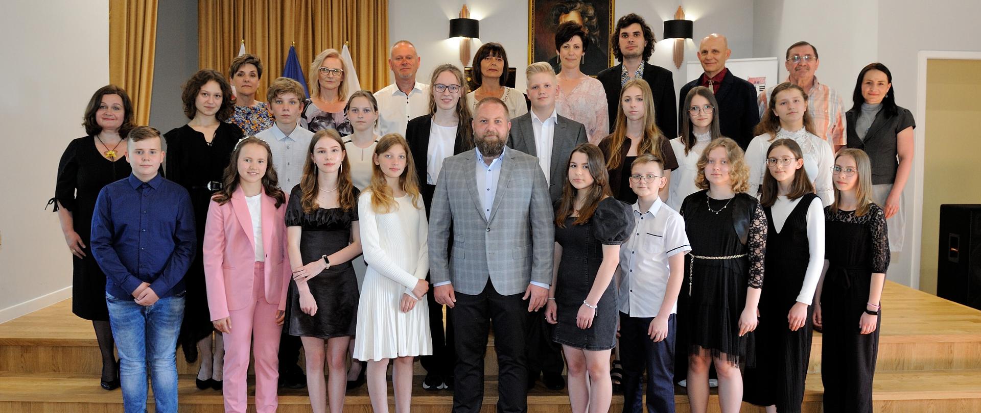 Zdjęcie wykonane w sali koncertowej PSM I st. w Miastku podczas koncertu absolwentów. Na zdjęciu 16 absolwentów wraz z kadrą pedagogiczną