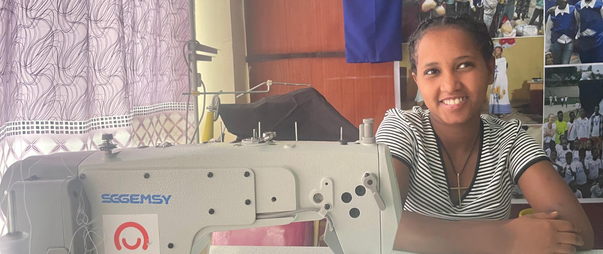 Kobieta siedzi przed maszyną do szycia z naklejką Polska pomoc