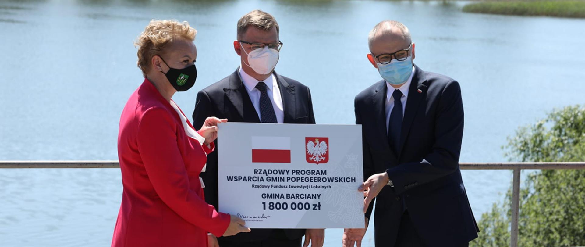 Wiceminister Błażej Poboży wraz z wojewodą warmińsko-mazurkim Arturem Chojeckim wręczają promesy.