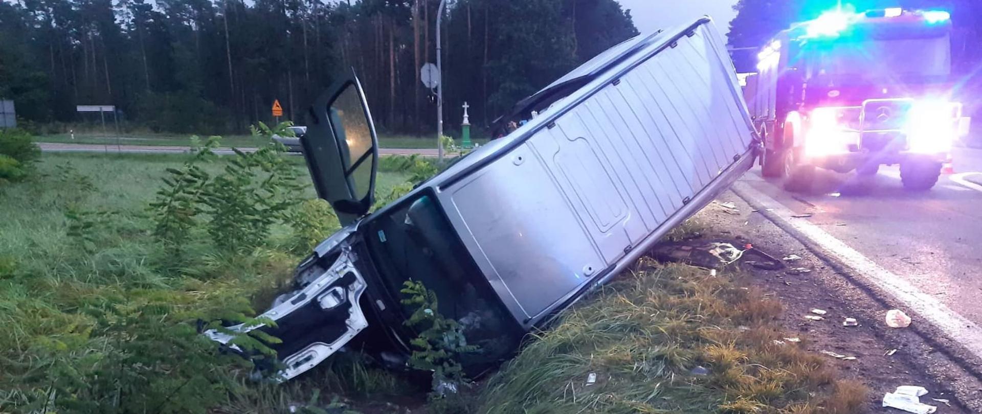 Wypadek na skrzyżowaniu dróg 74 i 728. Samochód dostawczy w rowie po lewej wbity przodem, tył uniesiony. Zniszczony przód auta. Po prawej za nim wóz strażacki zabezpiecza drogę.