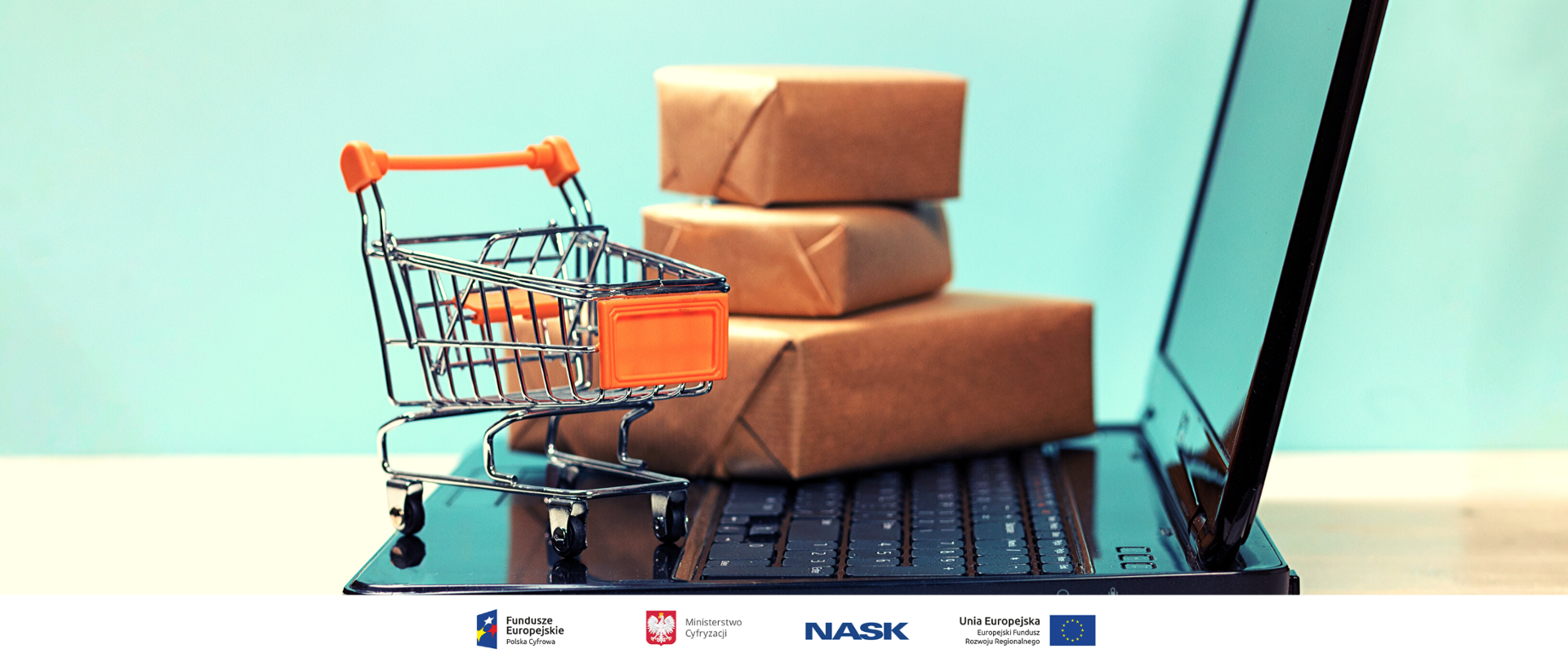 Laptop. Na klawiaturze leżą (jedna na drugiej) małe paczki, zapakowane w szary papier. Obok mini wózek sklepowy.